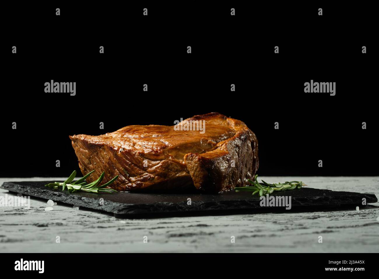 Bistecca di manzo con rosmarino su sfondo nero con spazio aperto per il testo design o menu del ristorante. Foto orizzontale Area di testo nera. Foto Stock