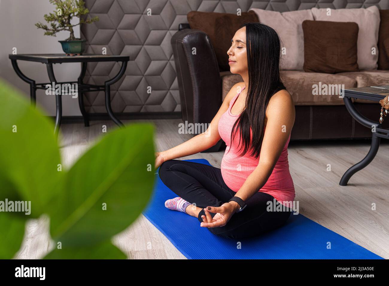 Donna giovane incinta rilassata che fa meditazione e yoga esercizi in casa Foto Stock