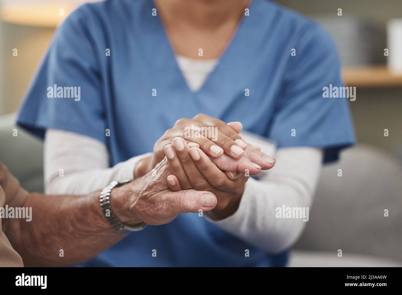Anche gli eroi indossano scrub. Shot di un'infermiera irriconoscibile che tiene una mano del paziente durante un controllo a casa. Foto Stock