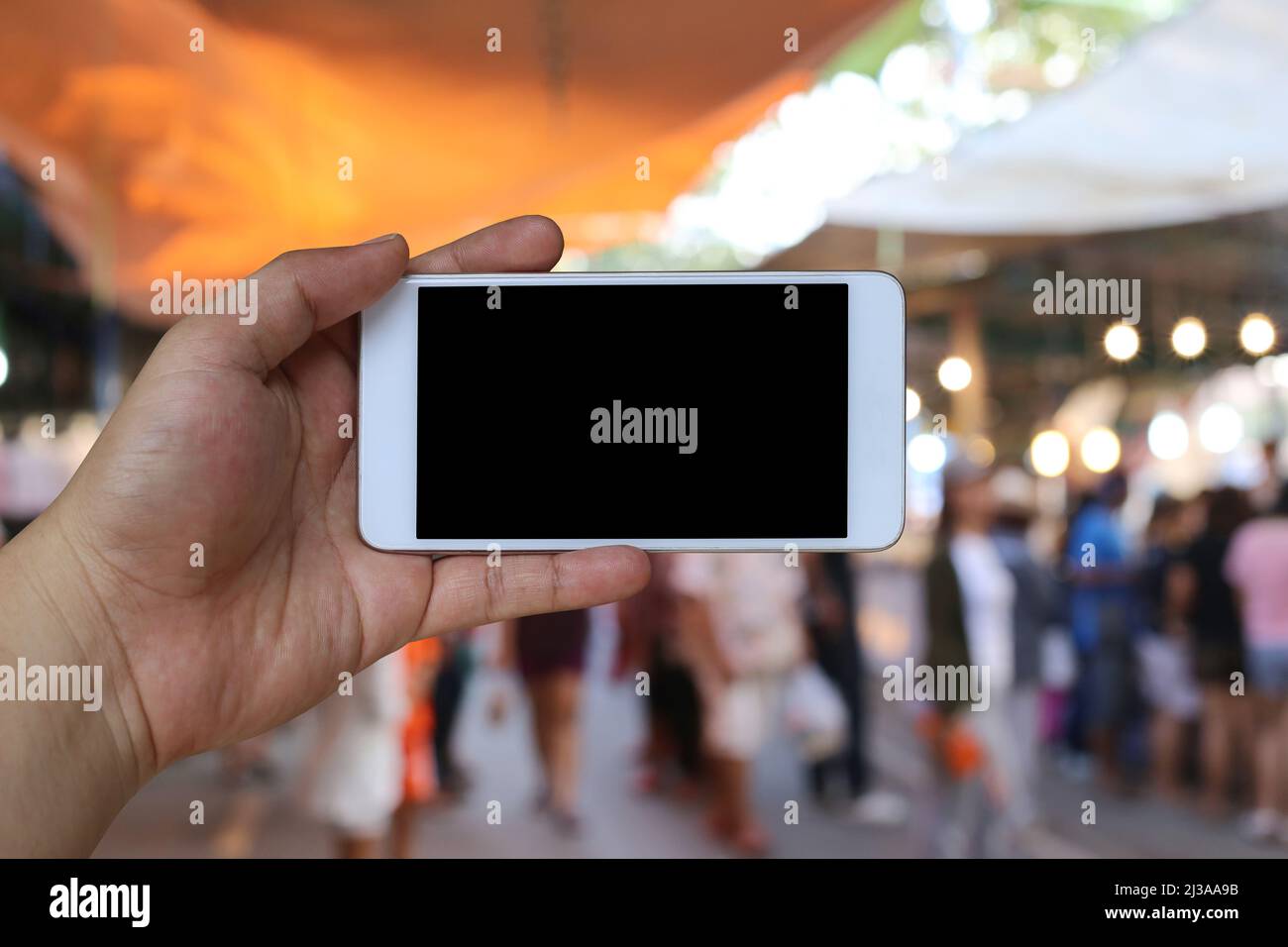 Mano di un uomo che tiene il dispositivo dello smartphone sullo sfondo del mercato degli acquisti e ha uno spazio di copia bianco sullo schermo. Foto Stock