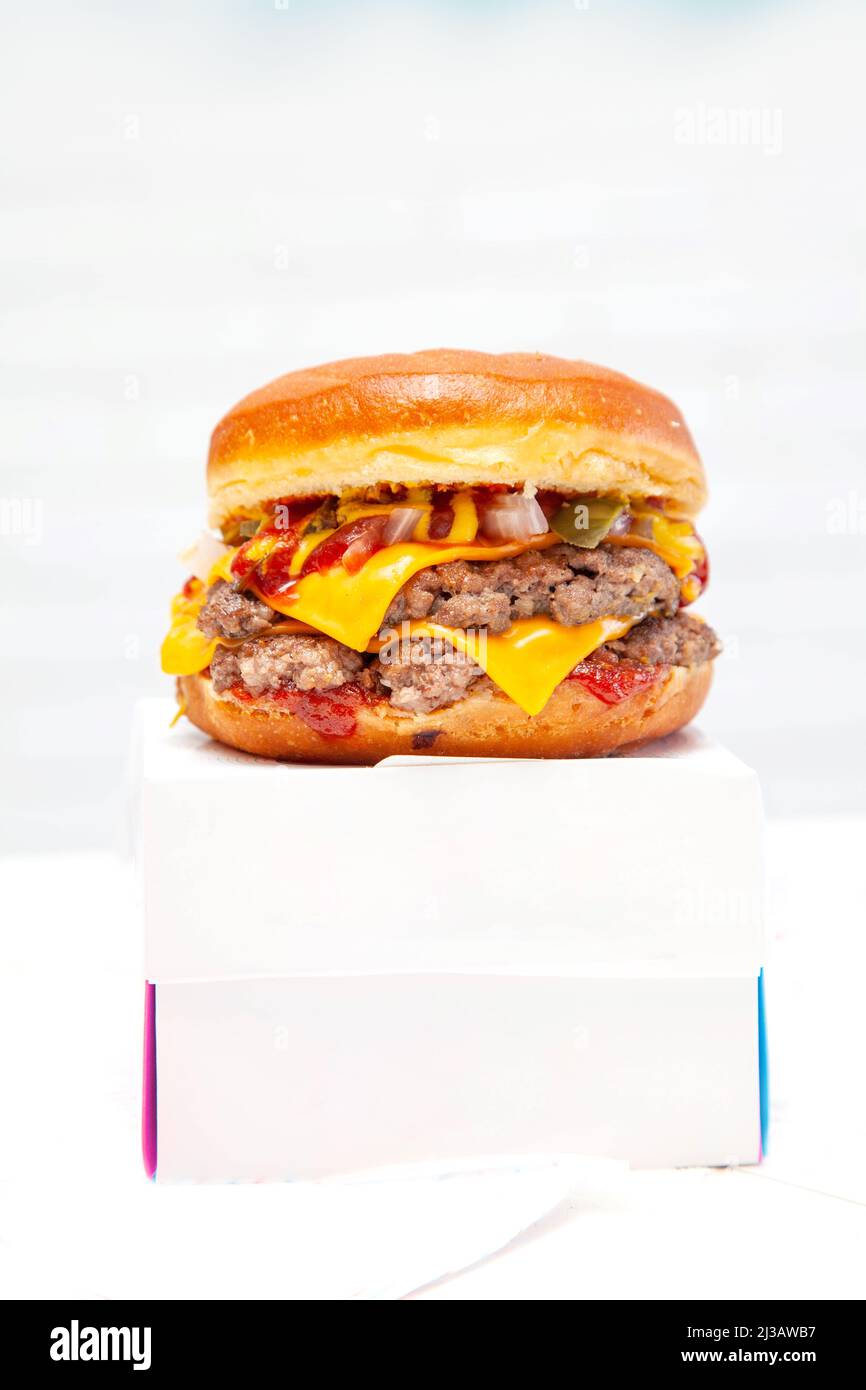 Hamburger con ciambelle a due piani con polpettine di manzo e condimento in cima a una scatola da asporto. Foto Stock