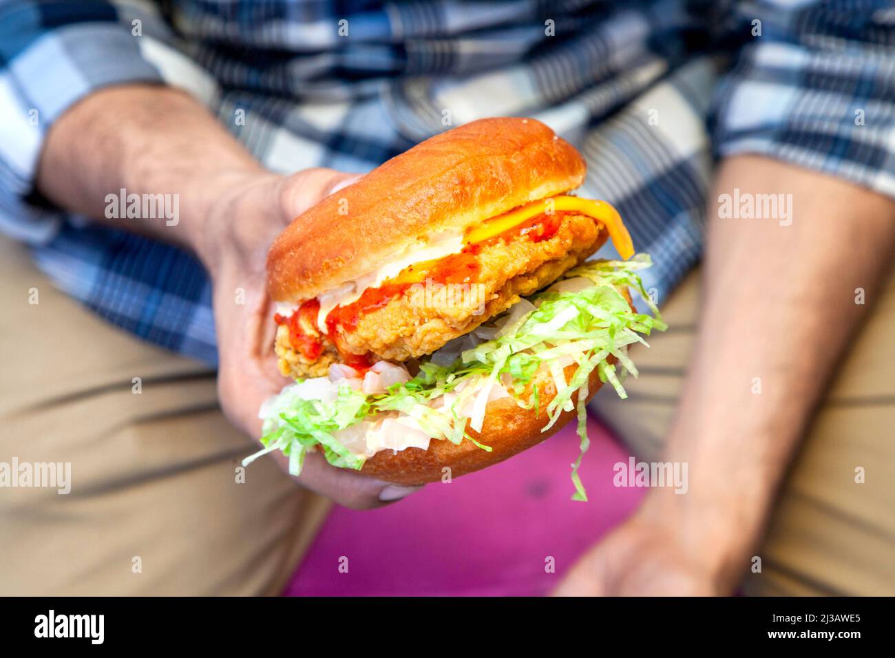 Hamburger di strada di pollo fritto succosa che tiene in un primo piano con una persona sullo sfondo Foto Stock