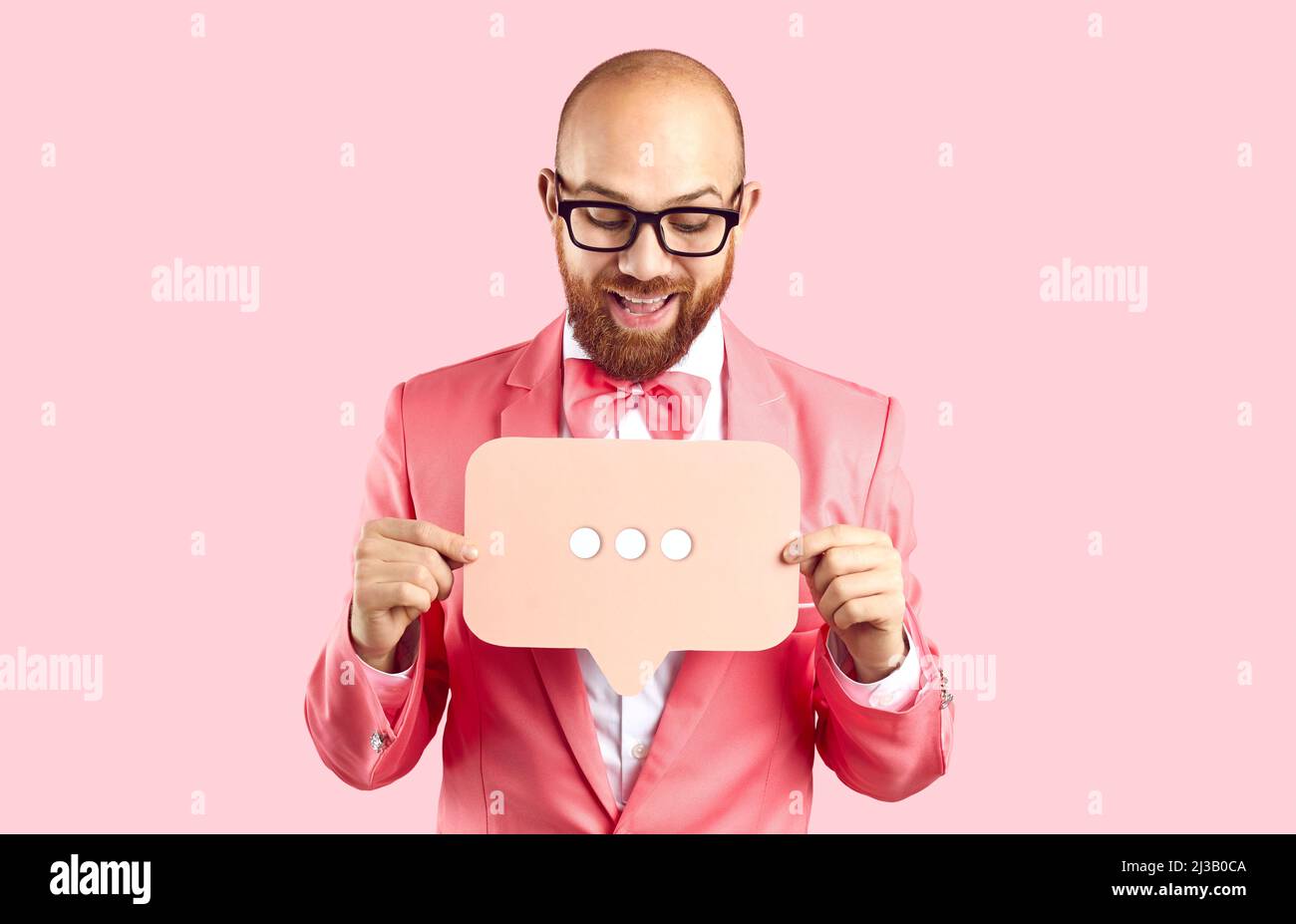 Positivo divertente uomo che tiene bolla parlare segno con tre punti isolato su sfondo rosa pastello. Foto Stock