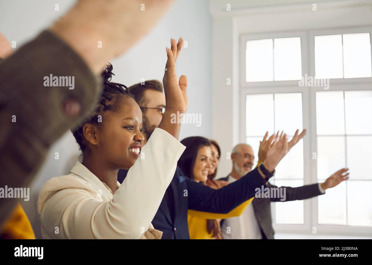 Pubblico felice multirazziale alzando le mani per fare domande alla conferenza o seminario Foto Stock