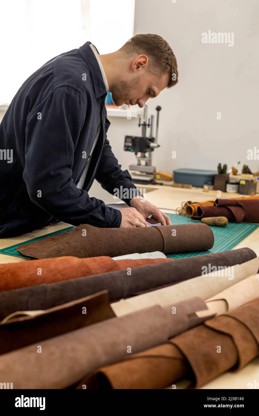 Tanner maschio che fa schema di taglio di borsa che lavora in officina di cuoio. Creazione artigianale Foto Stock