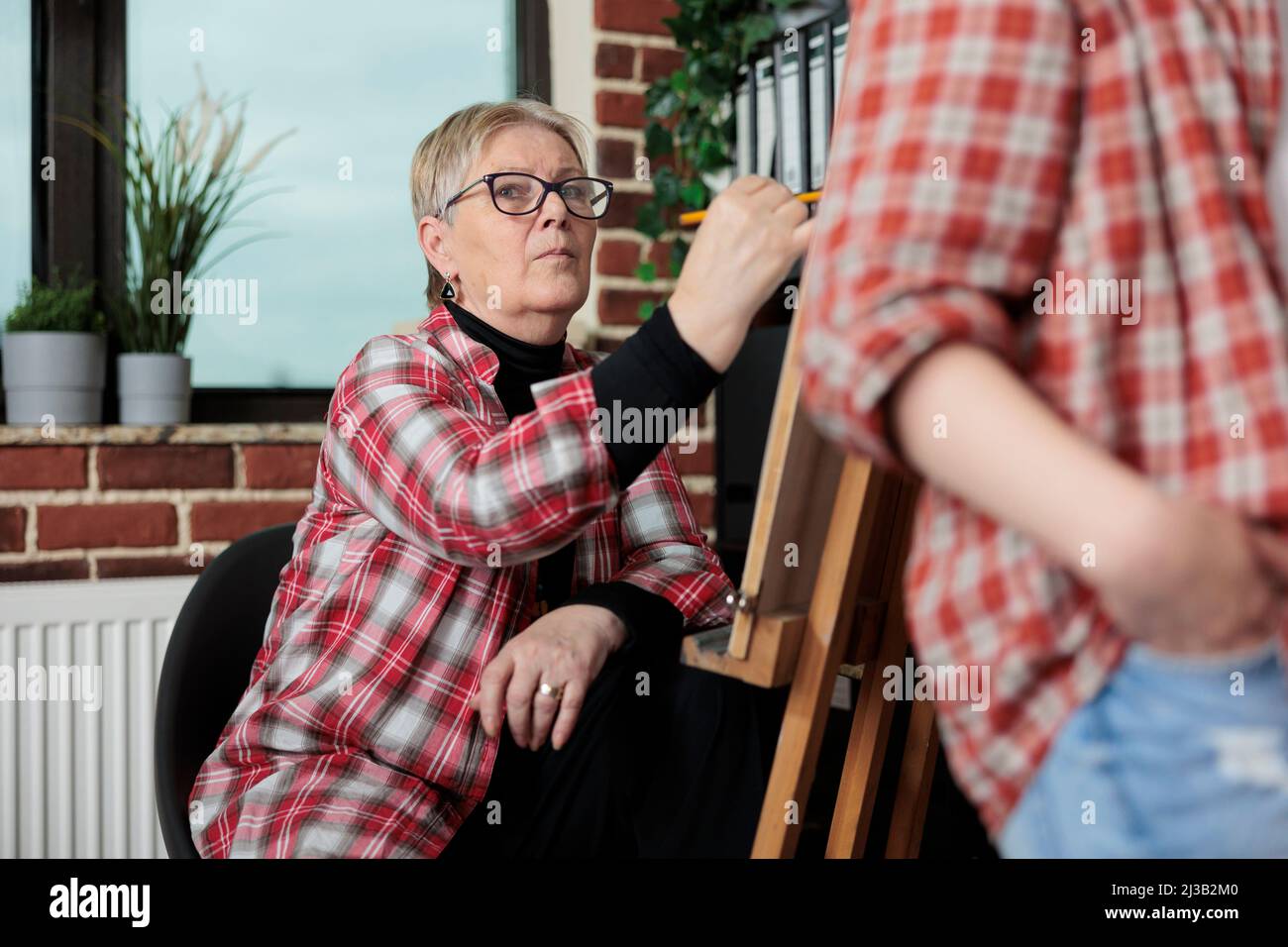 Ritratto di insegnante di artista senior che disegna vaso su tela utilizzando matita grafica durante la classe d'arte in studio muro di mattoni. Gruppo di artisti che lavorano all'educazione creativa studiando tecnica artistica Foto Stock