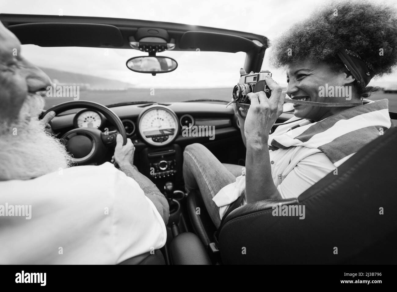 Coppia anziana felice divertirsi in auto convertibile durante le vacanze estive - concentrarsi sulla mano donna che tiene la fotocamera vintage Foto Stock