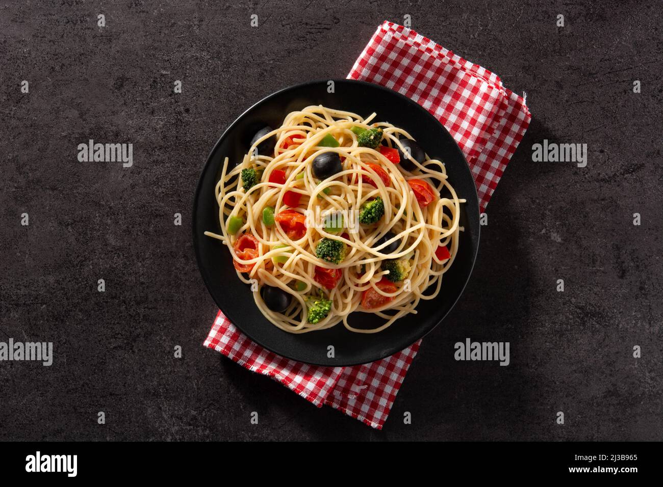 Spaghetti con verdure (broccoli, pomodori, peperoni) su sfondo nero Foto Stock