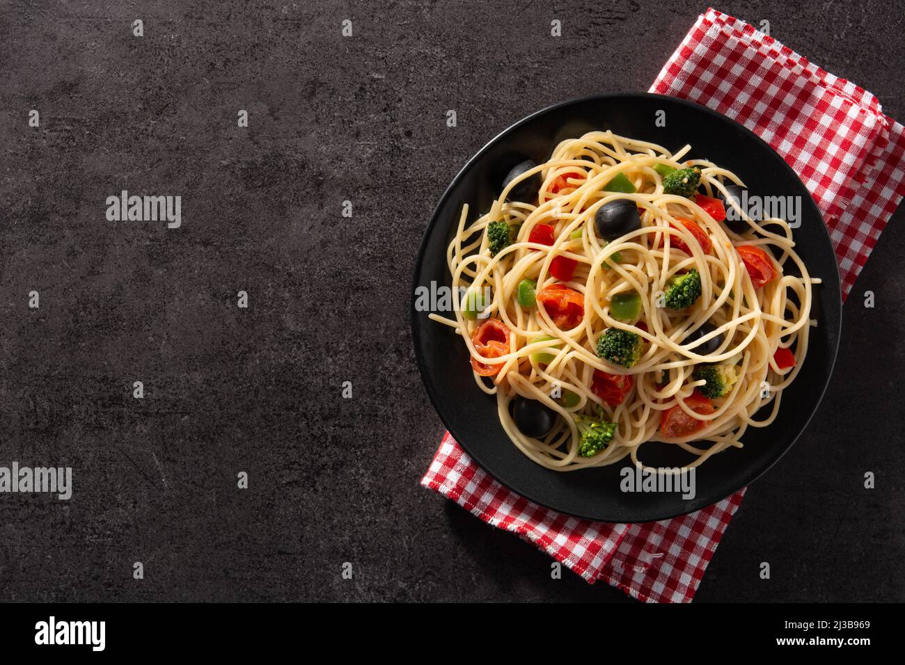 Spaghetti con verdure (broccoli, pomodori, peperoni) su sfondo nero Foto Stock