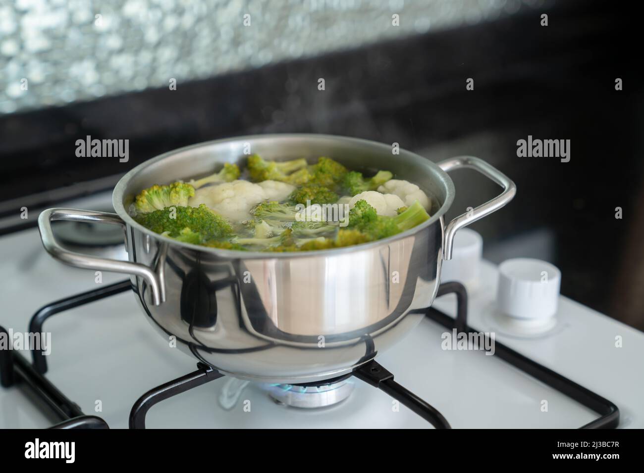 I broccoli freschi verdi vengono cotti in acqua in una pentola d'argento metallico su una stufa a gas bianca. Processo di cottura delle verdure. Foto Stock