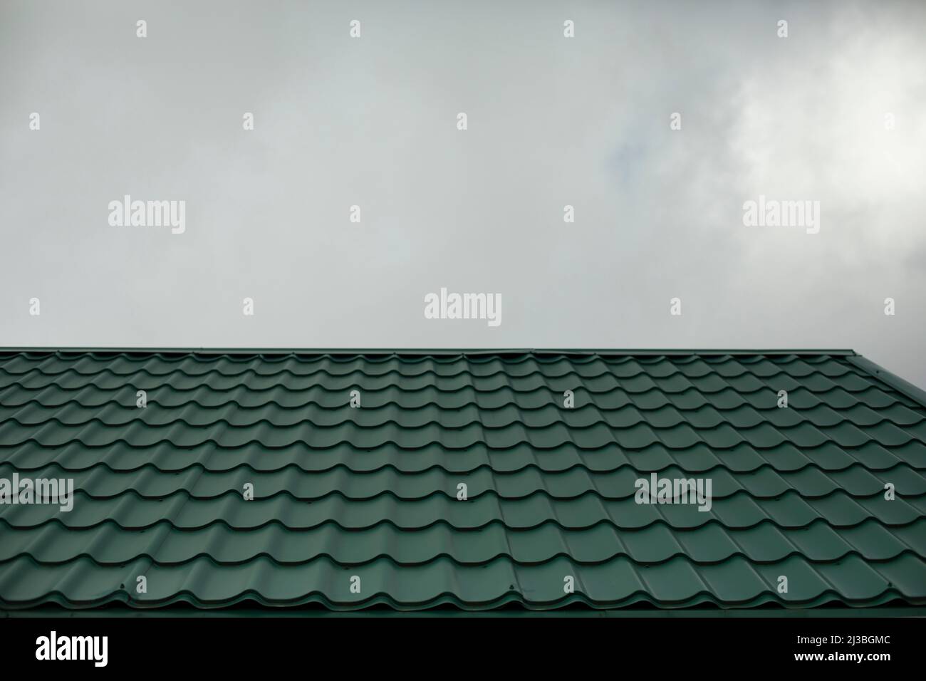 Tetto di casa sullo sfondo del cielo grigio. Tegole verdi. Dettagli dell'architettura. Foto Stock