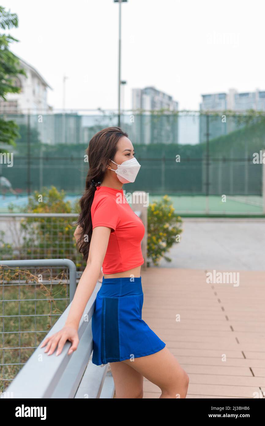 Graziosa giovane donna asiatica che indossa una maschera da tennis in piedi vicino al campo da tennis. Foto di alta qualità Foto Stock