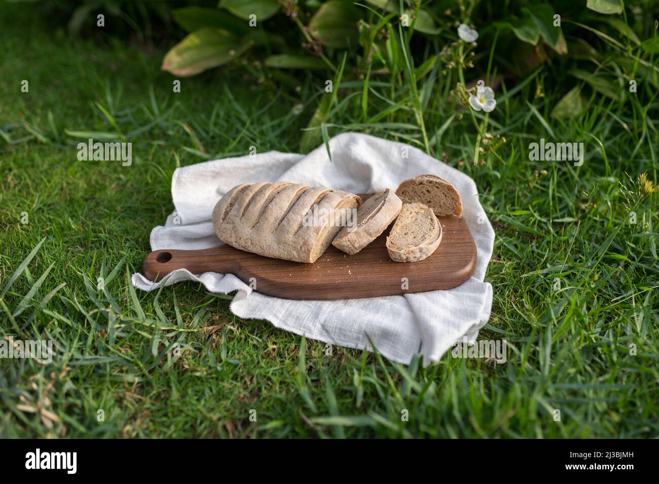 Composizione del pane fatto in casa con farina bianca su tavola di legno con tovagliolo bianco sull'erba verde. Foto di alta qualità Foto Stock