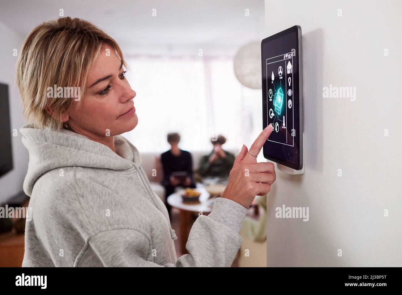 Donna che utilizza un'applicazione per la casa intelligente su un tablet montato a parete Foto Stock