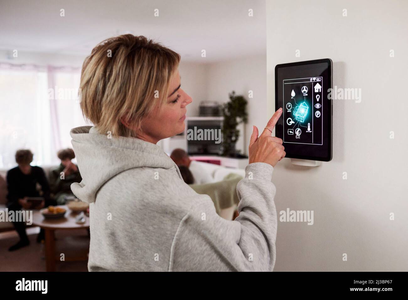 Donna che utilizza un'applicazione per la casa intelligente su un tablet montato a parete Foto Stock