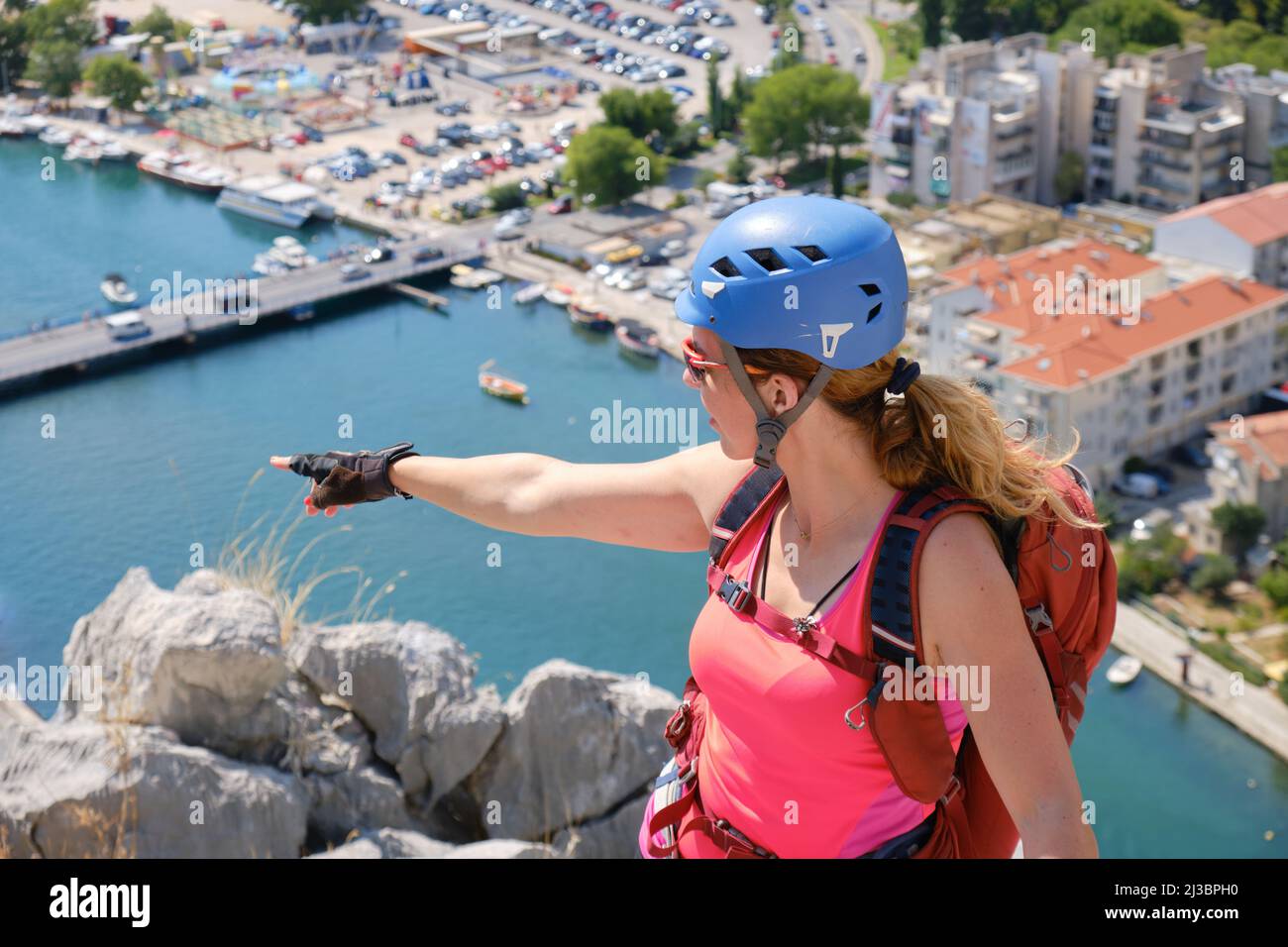 Donna scalatore su via ferrata Fortica punta il dito verso il fiume Cetina e Omis città, Croazia. Arrampicatore, verticale, avventura, attivo, estate, tour Foto Stock