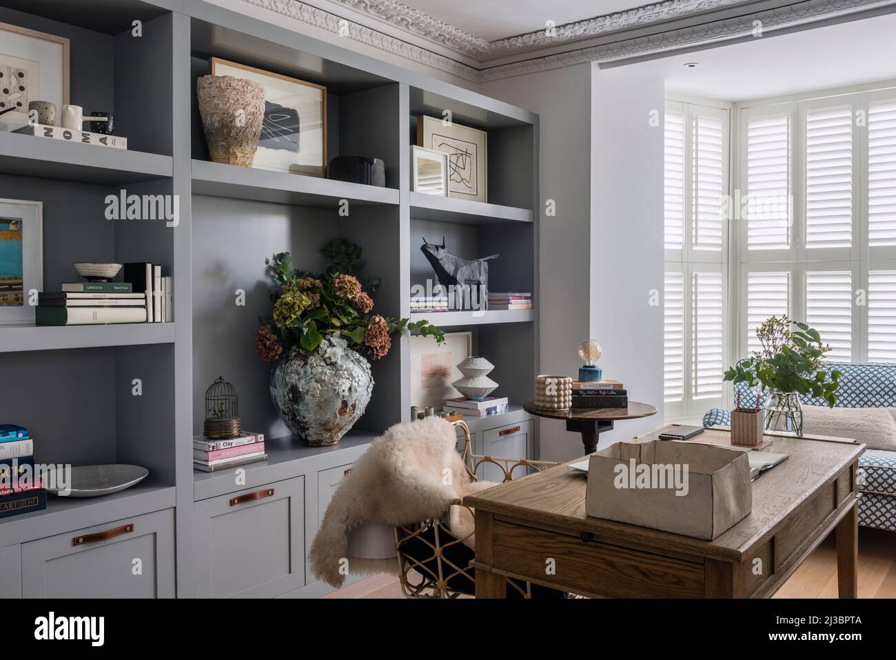 Libri e ornamenti su scaffali con persiane chiuse in casa ristrutturata St Ives, Cornovaglia, Regno Unito Foto Stock