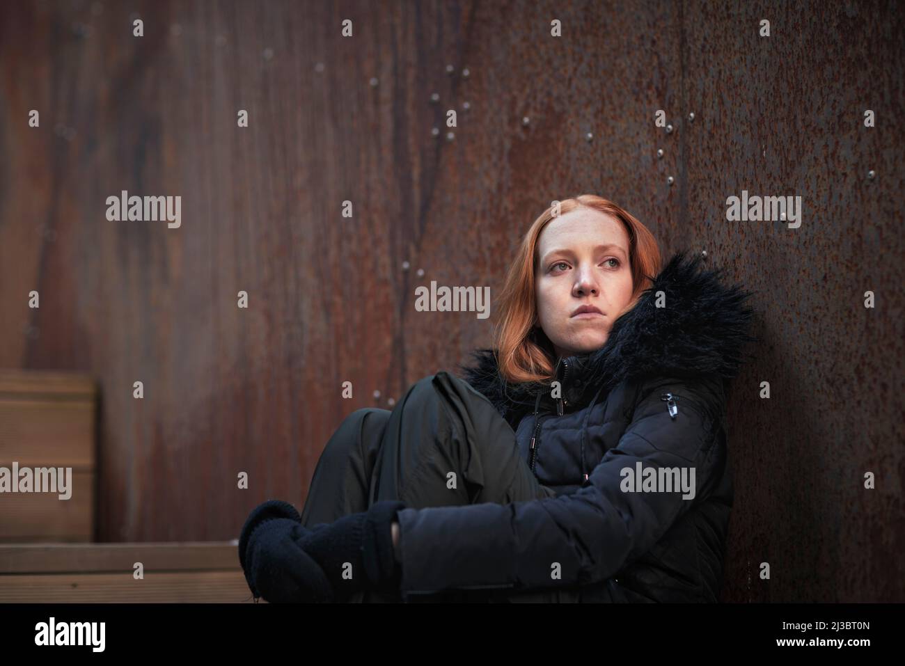 Giovane donna seduta contro il muro Foto Stock