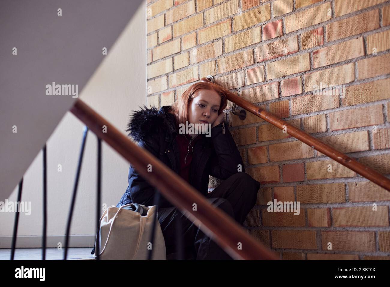 Giovane donna seduta sulle scale e appoggiata contro il muro Foto Stock