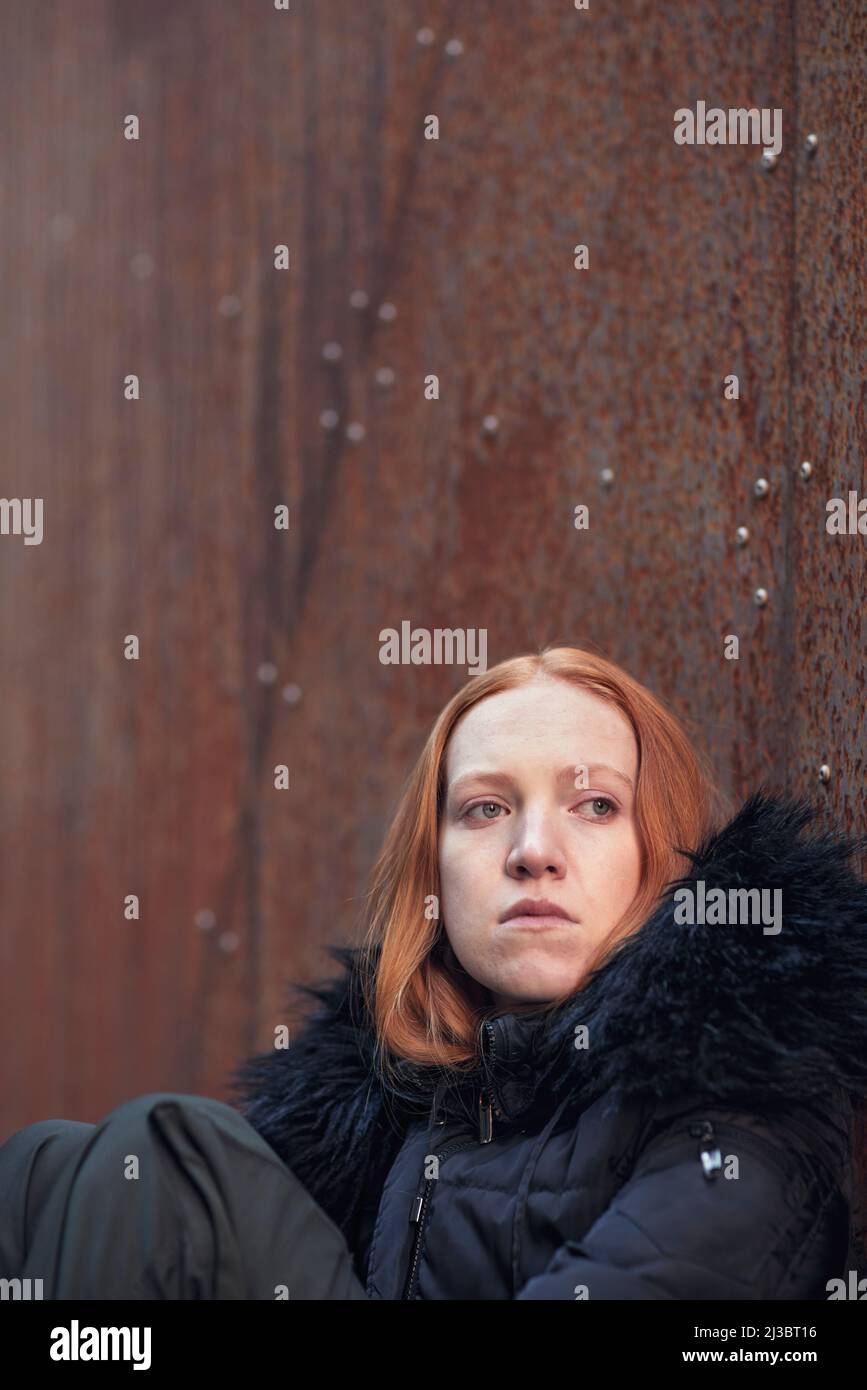 Giovane donna seduta contro il muro Foto Stock