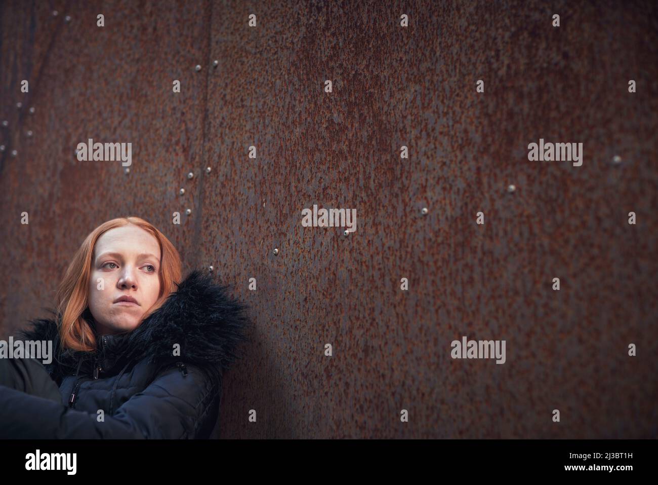 Giovane donna seduta contro il muro Foto Stock