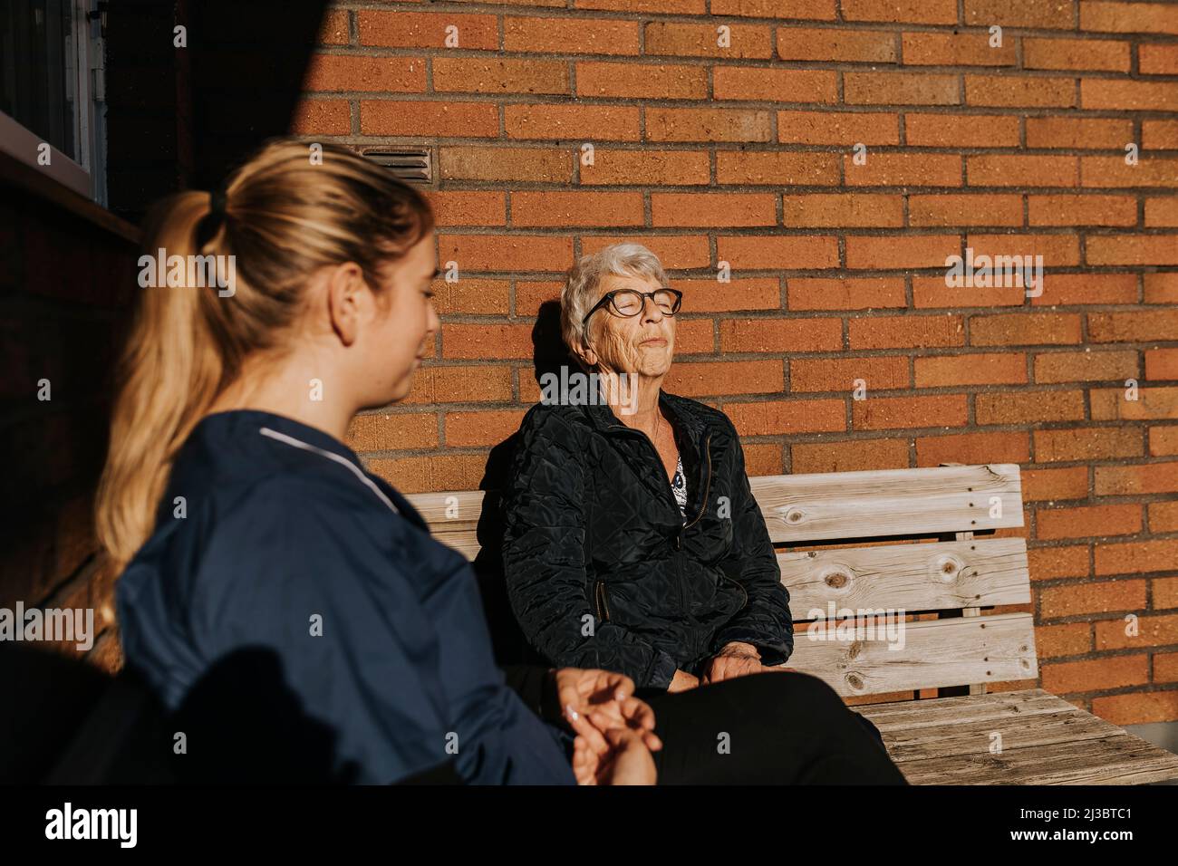 Casa custode e donna anziana seduta su panca e sole Foto Stock