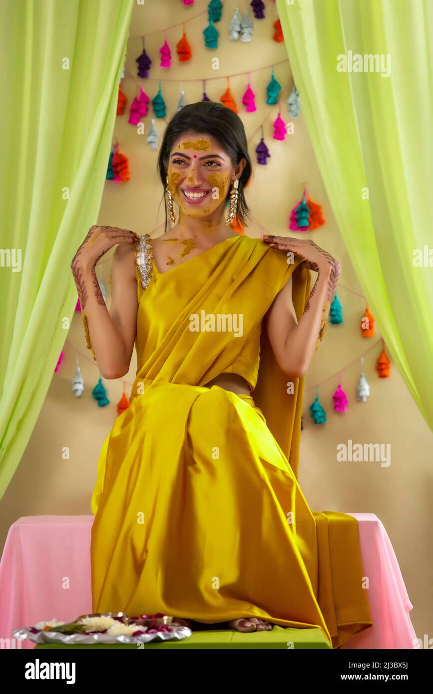 Ritratto di una sposa indiana seduta sul palco e posa con le mani a spalla sulla cerimonia haldi Foto Stock
