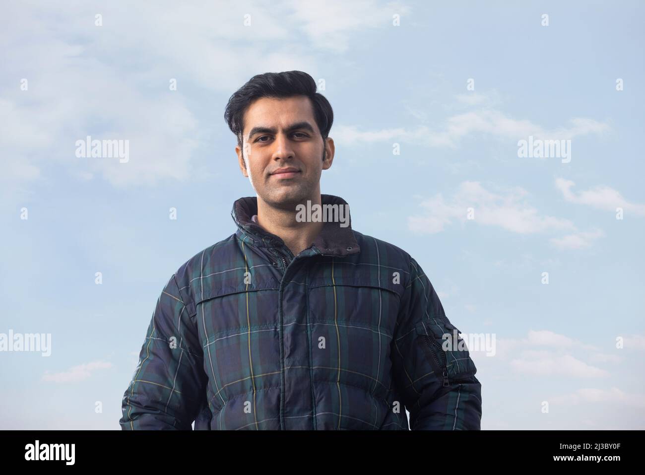 Ritratto di un giovane uomo in abito invernale in piedi sotto il cielo blu Foto Stock