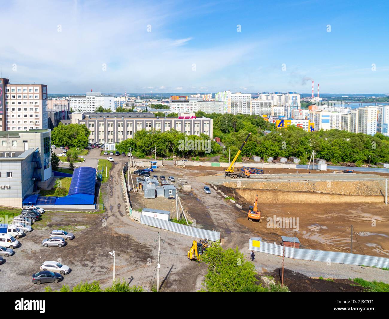 Kemerovo, Russia - 24 giugno 2021. Paesaggio urbano con edifici residenziali e un cantiere in primo piano, una zona industriale con fumo Foto Stock