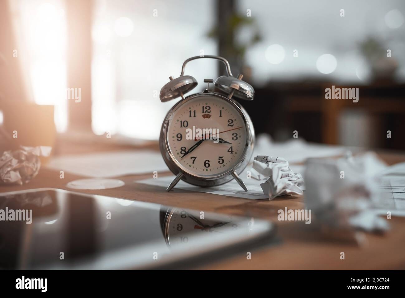È il momento di superare le scadenze imminenti. Foto vita di un orologio e carta sgualcita su una scrivania in un ufficio di notte. Foto Stock