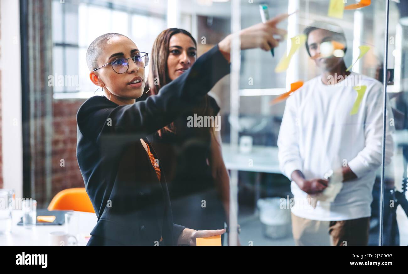 Donna d'affari intelligente che condivide le sue idee con il suo team. Giovane donna d'affari fiduciosa che condivide le sue note adesive con i suoi colleghi mentre si trova in posizione di fronte Foto Stock