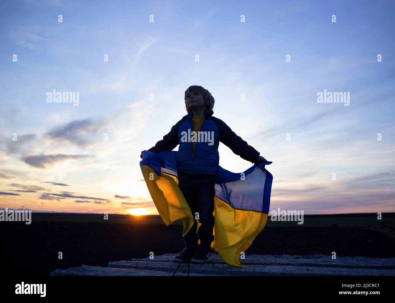 Silhouette di un ragazzo con la bandiera Ucraina sullo sfondo di un bel cielo al tramonto. Bambini contro la guerra. Il bambino patriota ucraino vuole la pace per Foto Stock