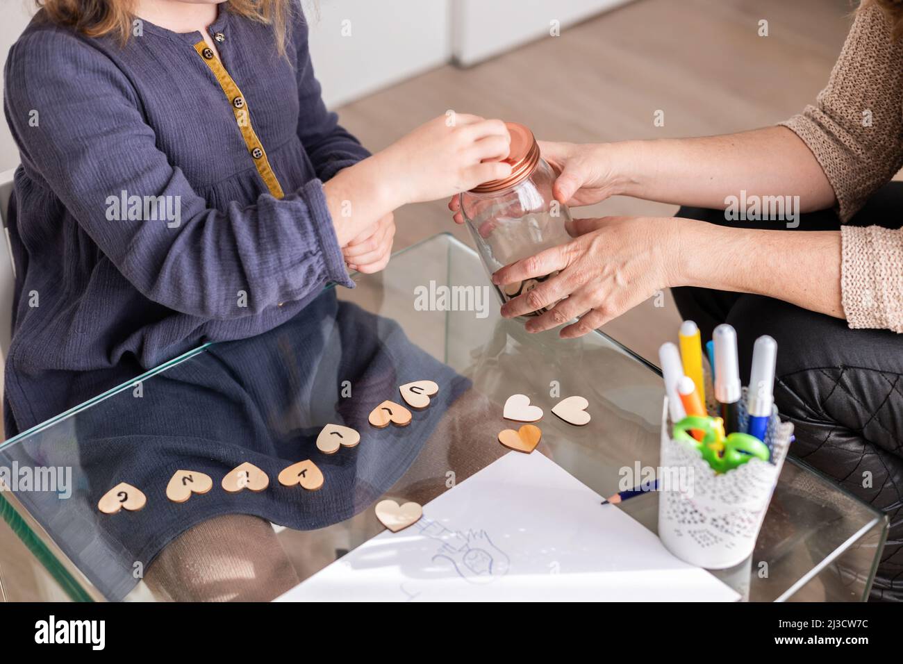 Ragazza ritagliata irriconoscibile che fa il desiderio con vaso di vetro piccoli cuori di legno mentre si siede vicino psicologo femminile Foto Stock