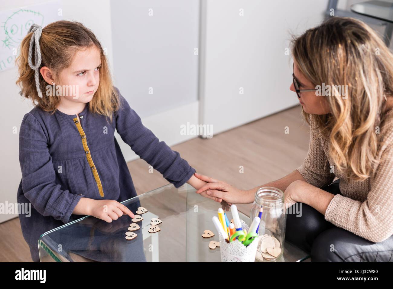 Cute girl making Help Me frase da piccoli cuori di legno vicino psicologo femminile mentre si guarda l'un l'altro i luce stanza Foto Stock