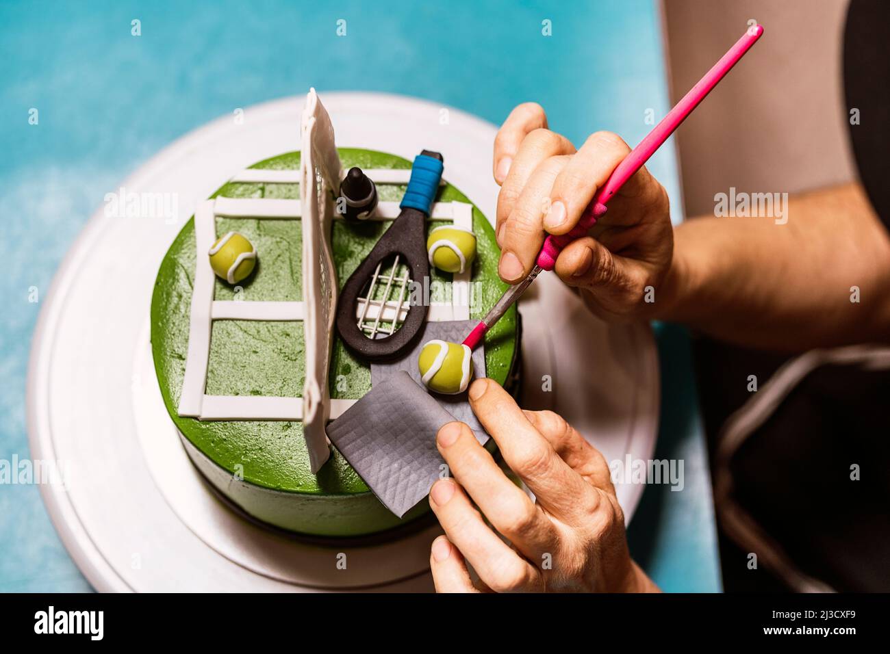 Da sopra raccolto Donna che organizza palle da tennis dolci vicino alla rete sulla torta fondante durante il lavoro in panetteria Foto Stock