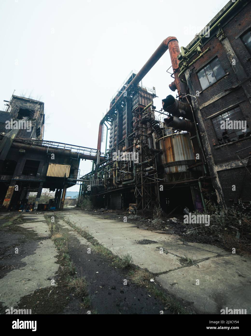 Da sotto tubi arrugginiti e silos situati all'esterno di impianti industriali desolati contro il cielo grigio Foto Stock
