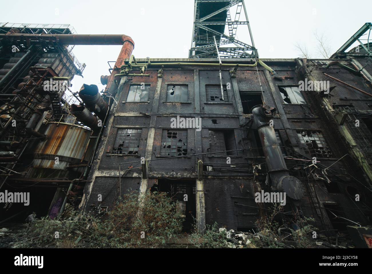 Da sotto tubi arrugginiti e silos situati all'esterno di impianti industriali desolati contro il cielo grigio Foto Stock
