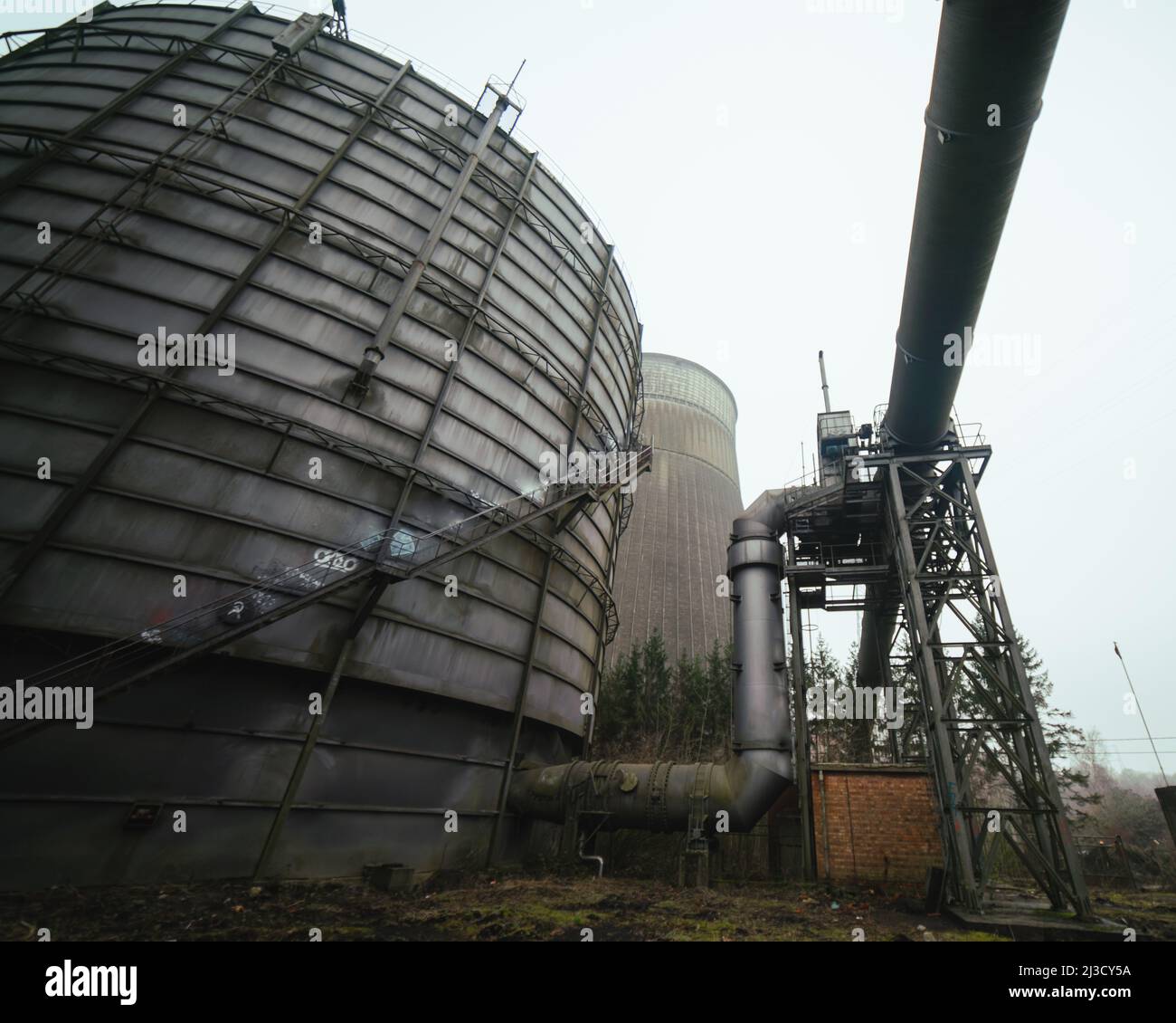 Da sotto tubi arrugginiti e silos situati all'esterno di impianti industriali desolati contro il cielo grigio Foto Stock