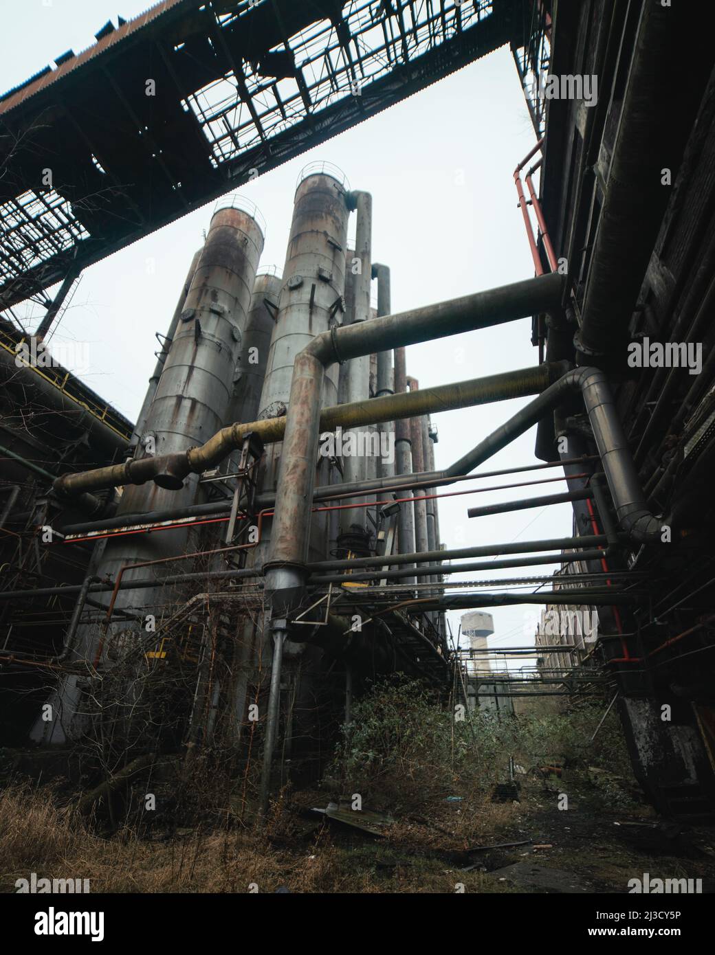 Da sotto tubi arrugginiti e silos situati all'esterno di impianti industriali desolati contro il cielo grigio Foto Stock
