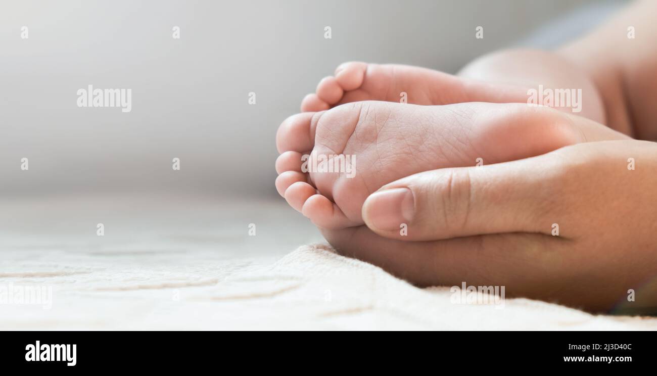 Madre che tiene i piedi del bambino nelle mani. Gambe Newborn in donna genitori mano. Piedi per bambini piccoli. Primo piano. Piccole dita del bambino. Festa della mamma Foto Stock