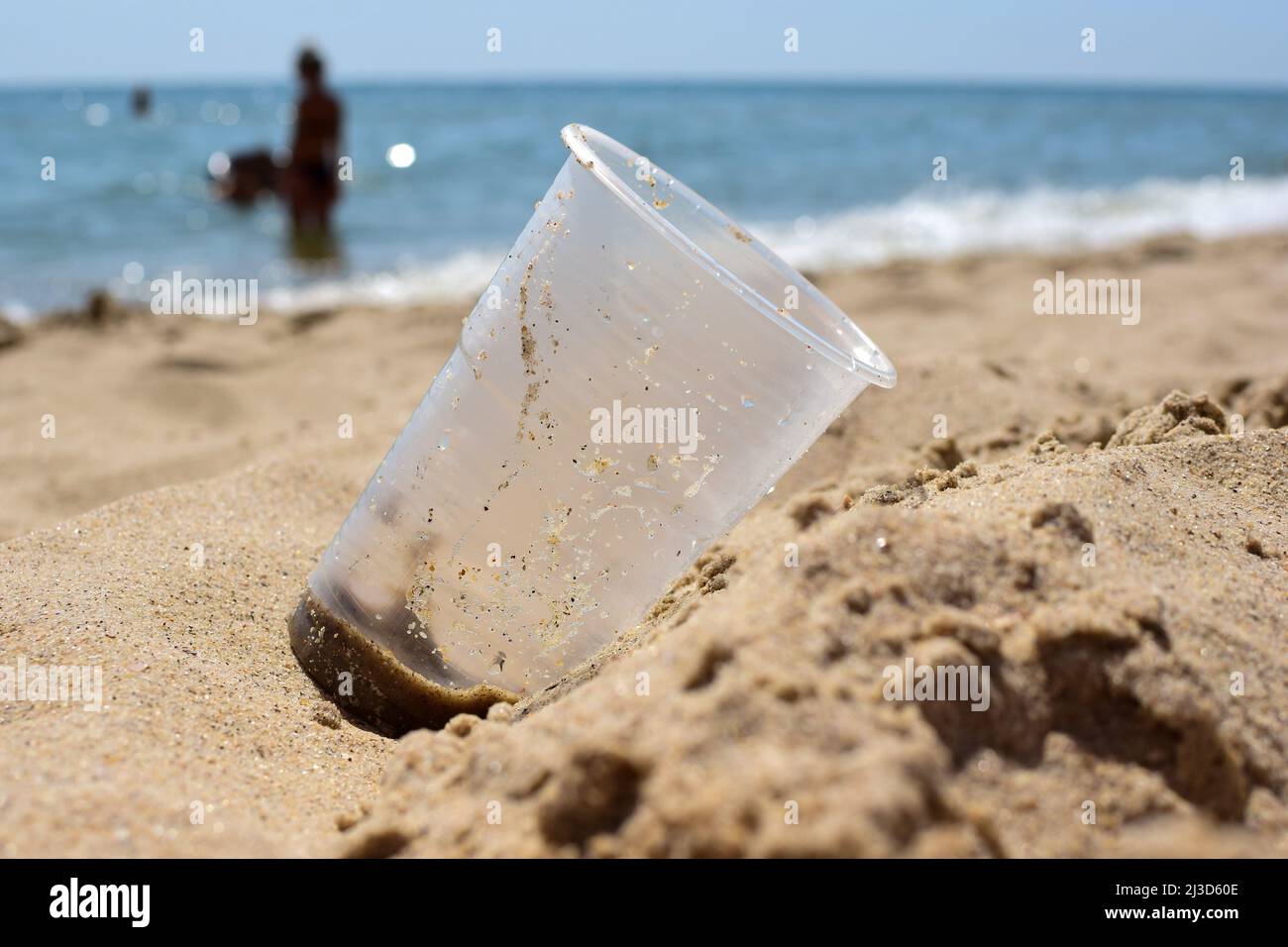 Sulla spiaggia sabbiosa del mare si trova un cristallo sporco in plastica primo piano. Lo sfondo è molto sfocato Foto Stock