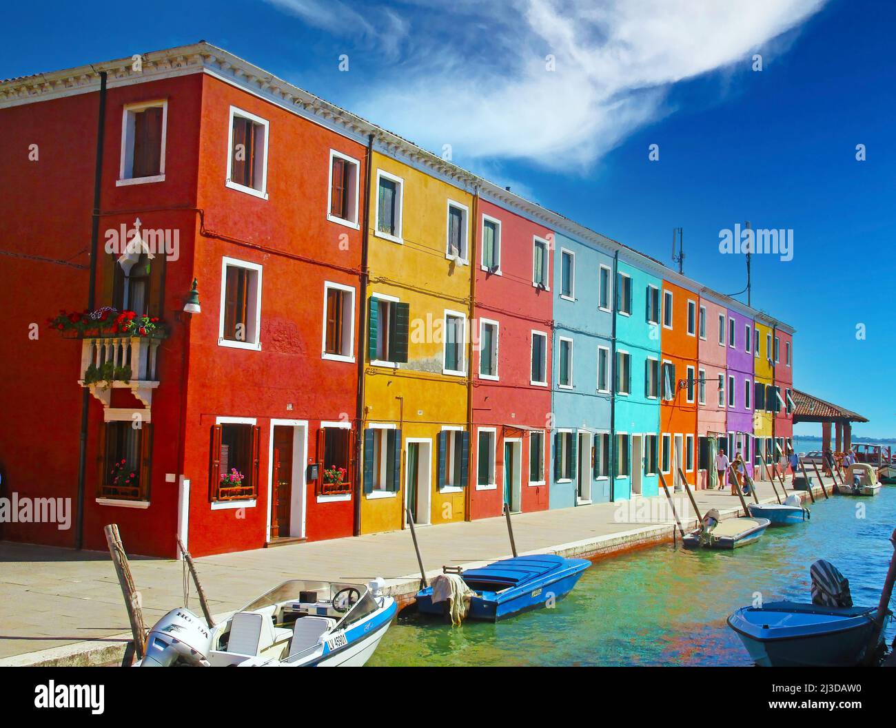 Venezia (burano), Italia - Maggio 9. 2019: Vista sulla fila di case sul lungomare multicolore luminose sul canale d'acqua con barche contro il cielo clearblue, nuvole fluide Foto Stock