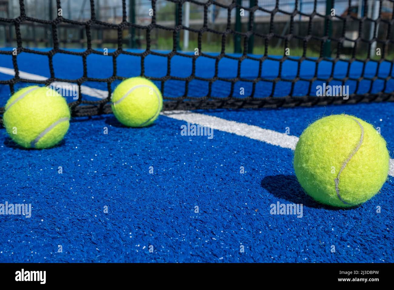 tre palle vicino alla rete su un campo da tennis con paddle blu Foto Stock