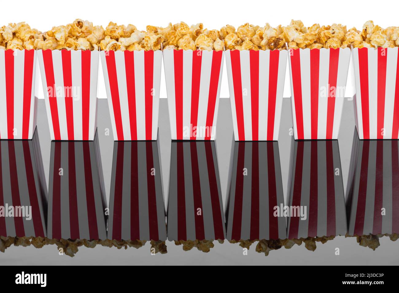 Cinema, cinema e teatro. Scatole di popcorn con strisce bianche e rosse piene di dolce con popcorn caramello su sfondo nero riflettente in bianco Foto Stock