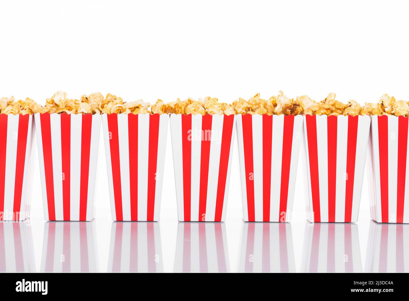 Cinema, cinema e teatro. Scatole di popcorn con strisce bianche e rosse piene di dolce con popcorn caramello su sfondo bianco riflettente in bianco Foto Stock