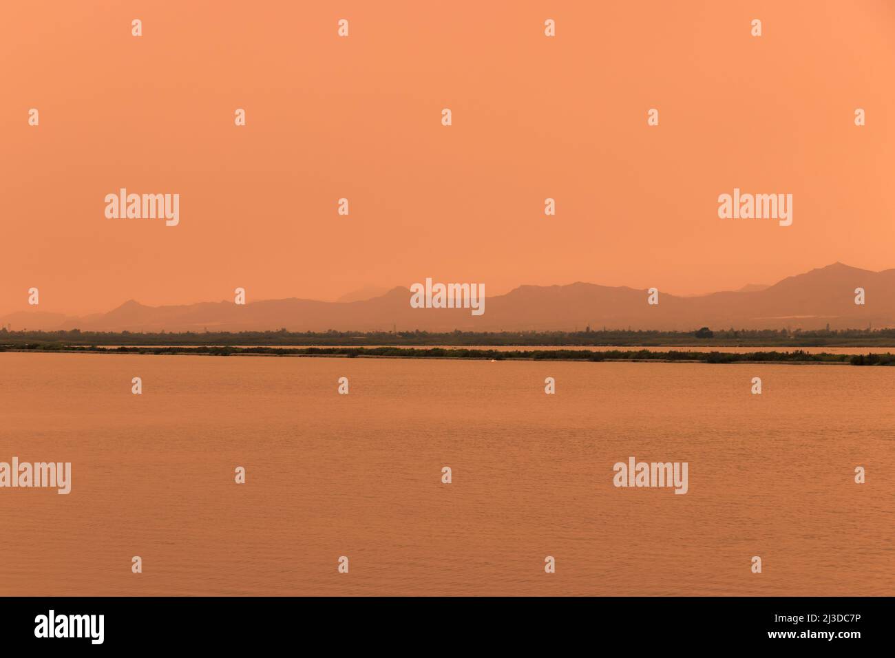 Tempesta di sabbia in Andalusia, Spagna. Cielo arancione, vista su una laguna e montagne sullo sfondo Foto Stock