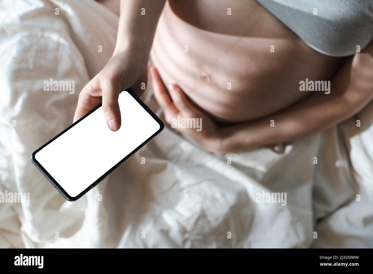 Una donna incinta usa uno smartphone con uno schermo vuoto mentre si rilassa nel suo letto di casa. Internet, shopping, comunicazione durante la gravidanza e prima della nascita di un bambino. Salute delle donne e dei neonati. Foto di alta qualità Foto Stock