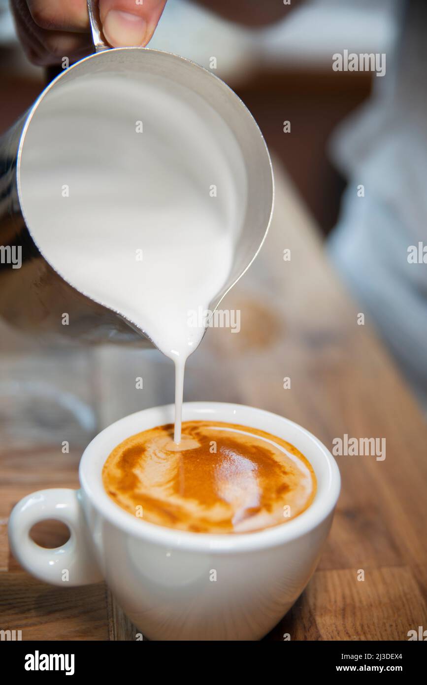 Preparazione del caffè in una caffetteria - versare il latte in un bianco piatto Foto Stock