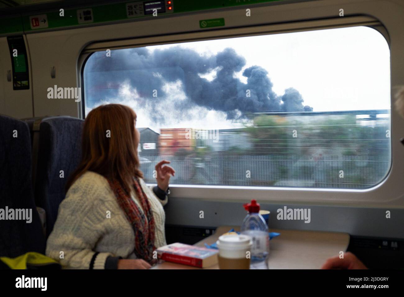 Donna GWR treno passeggero guardando fuori dalla finestra a fumo billowing dal fuoco a Southall West Londra il 5 aprile 2022 Inghilterra Regno Unito KATHY DEWITT Foto Stock