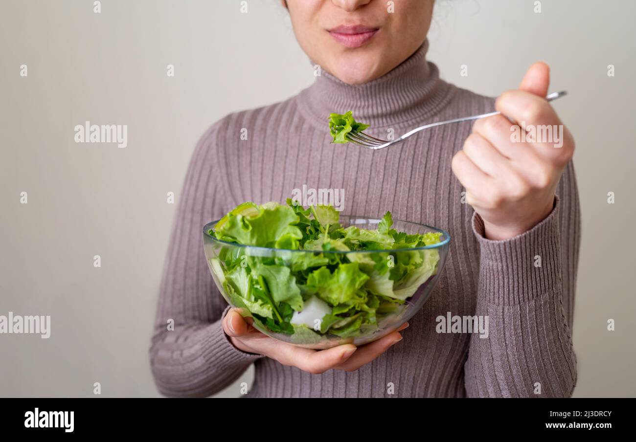 Primo piano foto di donna che mangia insalata mediteranneana con volto felice. Concetto di corretto piano nutrizionale e dieta per una vita sana. Messa a fuoco selettiva. Foto Stock